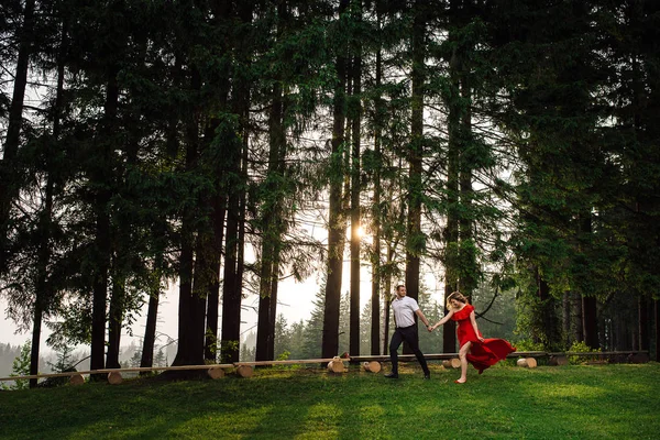Полнометражный снимок счастливой элегантной пары, держащейся за руки и бегающей по зеленому лесу во время заката . — стоковое фото