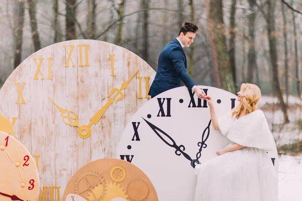 Feliz pareja de boda suavemente cogidos de la mano en los grandes relojes vintage en el bosque de otoño. Decoraciones creativas — Foto de Stock