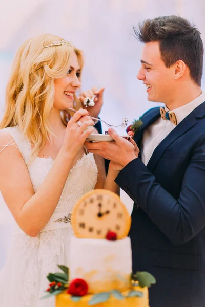 Bonito noivo alimentando sua bela noiva loira com bolo de casamento — Fotografia de Stock