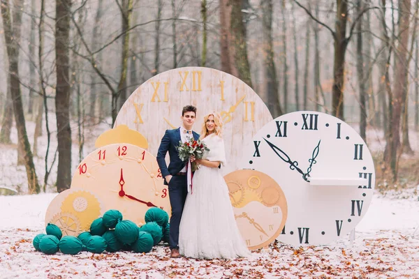 Feliz pareja de boda posando en los grandes relojes vintage en el bosque de otoño. Decoraciones creativas — Foto de Stock