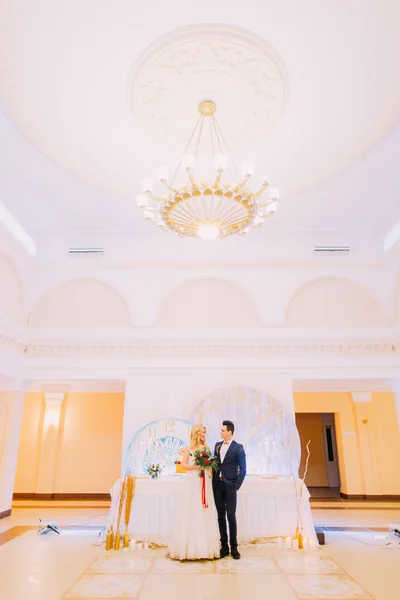 Glückliches junges Hochzeitspaar posiert mit Rosenstrauß im Restaurant. — Stockfoto