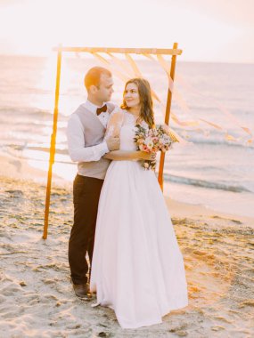 Yeni evliler günbatımı sırasında sahilde sarılma..