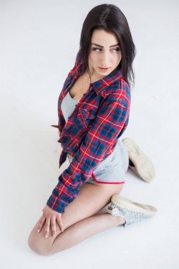 Genç çekici esmer kısa şort ve beyaz katta oturan ve uzağa bakarak hücre gömlek doğal makyajlı görünümünü yukarıda.