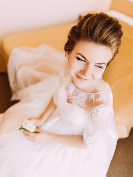 A noiva sorridente está segurando o mini-buquê branco e sentado na cama. O retrato acima . — Fotografia de Stock