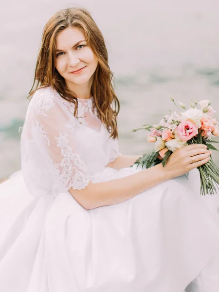 O retrato de close-up da noiva sentada e segurando o buquê de casamento consistia nas rosas coloridas no fundo do mar . — Fotografia de Stock