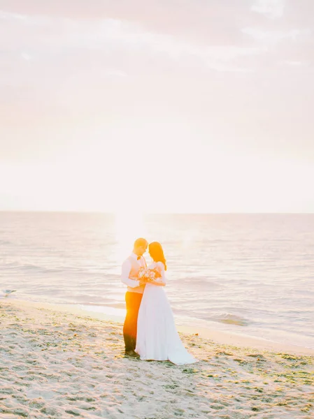 Mooie jonggehuwde paar is tijdens de zonsondergang op het strand knuffelen. — Stockfoto