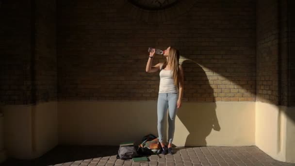 Genç kızın casual giyim içme suyu tuğla duvarın arka plan, şişe tam uzunlukta görünümü. — Stok video