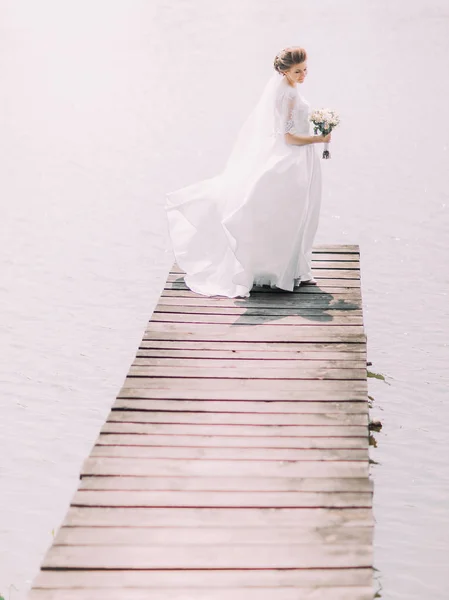 Боковой вид невесты с букетом, смотрящей на реку, стоя на пирсе . — стоковое фото