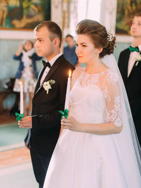 Newlyweds holding candles with green ribbons during the wedding ceremony. The side view. — Stock Photo, Image