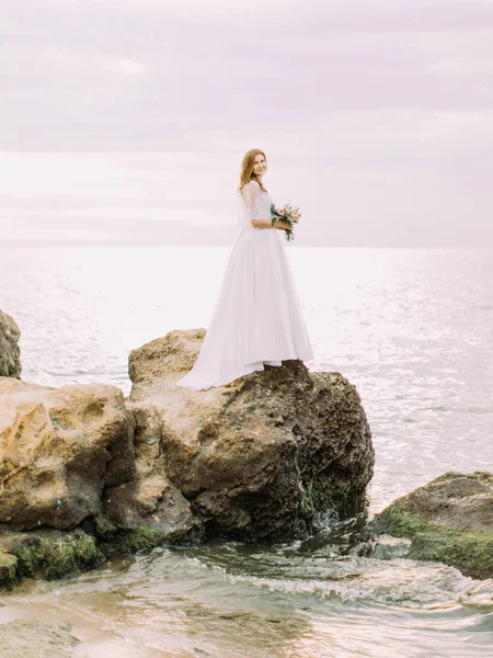 Az oldalnézet, a sedding csokor állt a kövön, mosott a tengerparton a menyasszony. — Stock Fotó