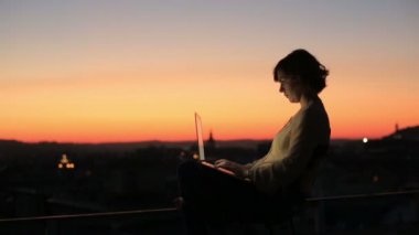 Bir sıcak güneşli gün açık havada bir dizüstü bilgisayar klavye yazarak bir iş kadını. Güzel bir şehir günbatımı arka plan