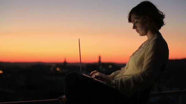 Femme tapant sur un clavier d'ordinateur portable par une chaude journée ensoleillée à l'extérieur. Belle ville coucher de soleil arrière-plan — Video