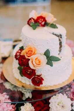 Beyaz düğün pastası dikey görünüm kırmızı ve turuncu gül ile dekore edilmiştir..