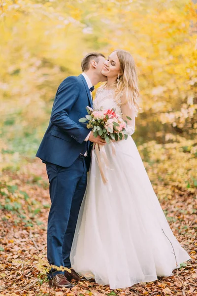 The groom is kissing the bride in the neck. Yellowed forest location. — Stock Photo, Image
