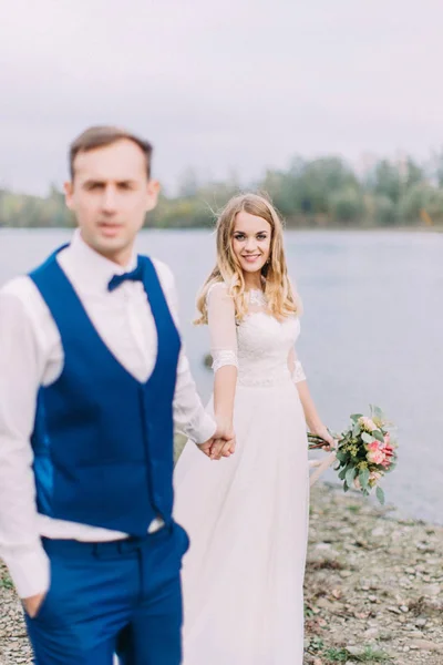 Vrolijke bruid volgt de bruidegom langs de kust. — Stockfoto