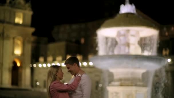 Bonito casal conversando e relaxando perto da fonte no centro de Roma. Retrato de belo casal sorridente apaixonado ficando perto da fonte à noite. Vídeo 4K . — Vídeo de Stock