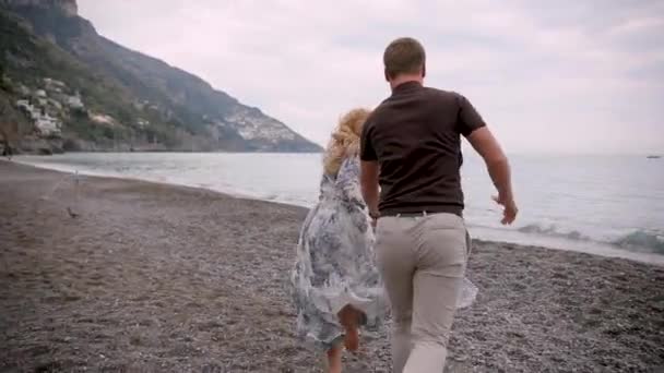 Video di coppia sulla spiaggia romantico tenersi per mano in esecuzione giocoso. Giovane coppia innamorata godendo romanticismo in abbigliamento casual elegante sulle vacanze al mare di lusso viaggi. Video 4K . — Video Stock