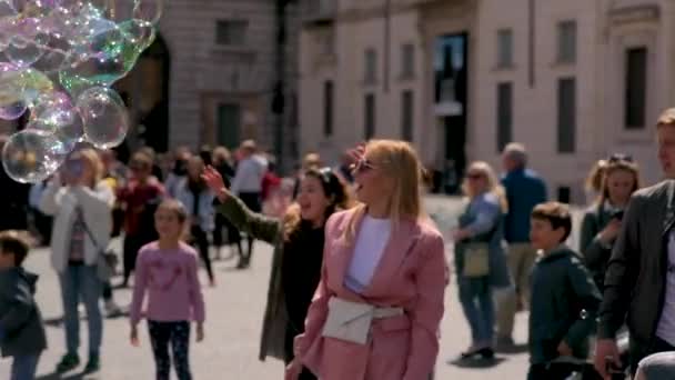 Video einer fröhlichen Frau, die auf dem Platz steht und mit anderen Menschen Seifenblasen fängt. Urlaub in Rom. 4k-Video. — Stockvideo