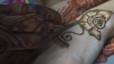 Process of henna tattoo. The artist is painting the mehendi on the female hands. Close-up view. No faces.