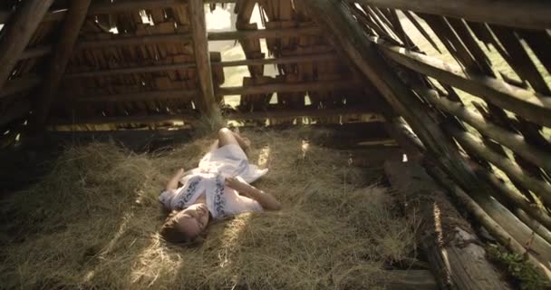 Ung kvinna leende i solen strålar på hö. Träskjul. 4k. — Stockvideo