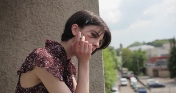 Portret di giovane donna bruna che fuma e pensa nel balcone. Città vecchia, tempo soleggiato, cattiva abitudine. Video 4K . — Video Stock