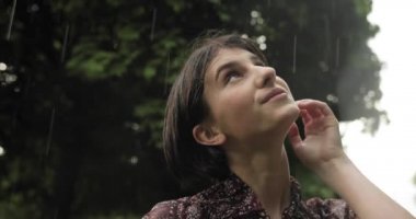 Happiness and rain. Close up video of brunette attractive woman smiles in the rain, the woman immersed in the nature under the rain. 4K video.