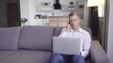 Takım elbiseli yakışıklı sarışın adam evde çalışıyor. İşadamı kanepede oturuyor, dizüstü bilgisayarda yazarken telefonla konuşuyor. Şık bir oturma odası..