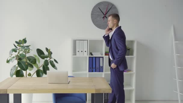 Seriöser Geschäftsmann im blauen Anzug telefoniert im schicken Büro. Konzentrierter und gestresster Mann telefoniert emotional am entfernten Arbeitsplatz. — Stockvideo