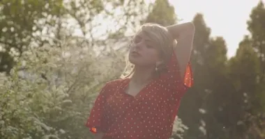 Muhteşem altın sarısı saçları olan genç ve çekici bir kadın çiçek açan güzel bir ağaçta dolaşıyor. Çekici genç bayan güneşli bir günde doğada dinleniyor. 4k video.