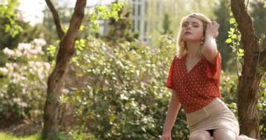 İnanılmaz güzel sarışın kız güzel bir yaz parkında bankta oturuyor. Muhteşem altın saçlı çekici bir kadın doğadan zevk alıyor. Bakışlarıyla büyülüyor. 4k