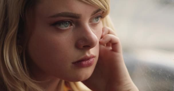 Közelkép egy fiatal, figyelmes nőről, aki kinézett az ablakon. Bájos hölgy, gyönyörű arany hajjal, piros blúzban. 4k videó — Stock videók