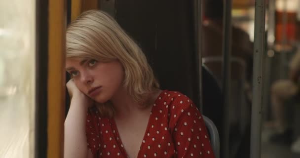 Tramvayda otururken pencereden dışarı bakan genç yorgun kadının portresi. Kırmızı bluzlu, muhteşem altın sarısı saçları olan hoş bir bayan. 4k video — Stok video