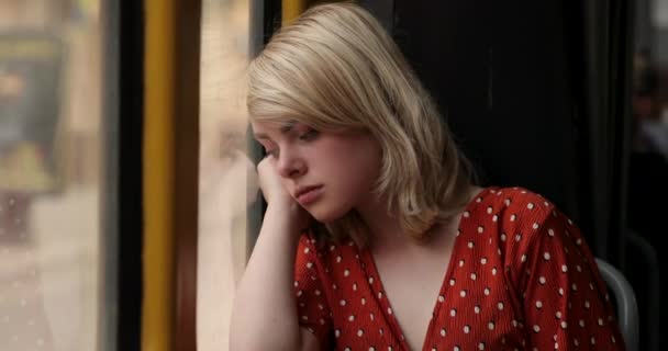 Retrato de una joven mujer cansada mirando por una ventana, mientras está sentada en el tranvía. Encantadora dama con un magnífico cabello dorado en blusa roja. Vídeo 4K — Vídeos de Stock