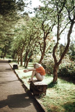 Ağaçların yanındaki bankta oturan güzel bir kadın, dışarıda dinlenen güzel bir kız. Yumuşak yeşil renkler. Park