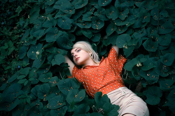 Hermosa mujer acostada entre plantas de color verde oscuro, chica bonita relajante al aire libre . — Foto de Stock