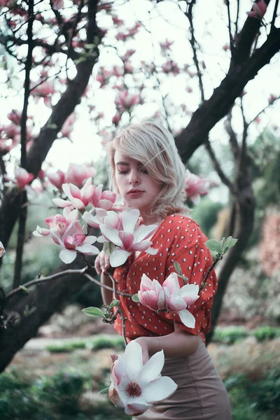 Hermosa mujer de pie entre ramas de sakura, chica bonita relajante al aire libre. Colores rosados suaves — Foto de Stock