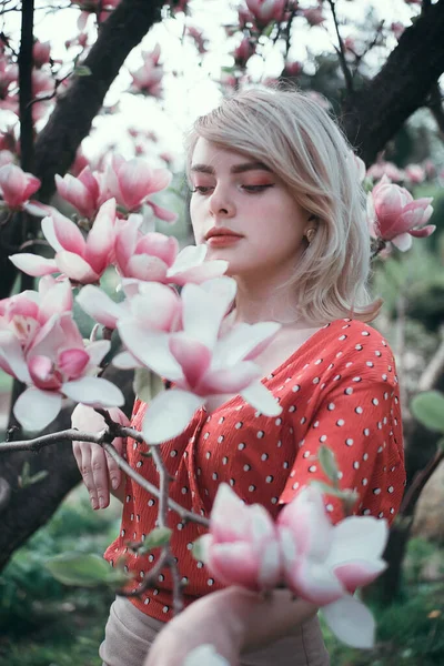 Hermosa mujer de pie entre ramas de sakura, chica bonita relajante al aire libre. Colores rosados suaves. Primer plano . Imagen De Stock