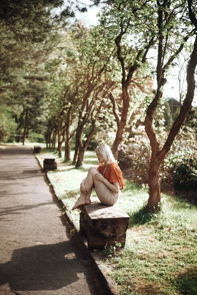 Mulher bonita sentada no banco perto das árvores, menina bonita relaxante ao ar livre. Cores verdes suaves. Parque Fotografias De Stock Royalty-Free