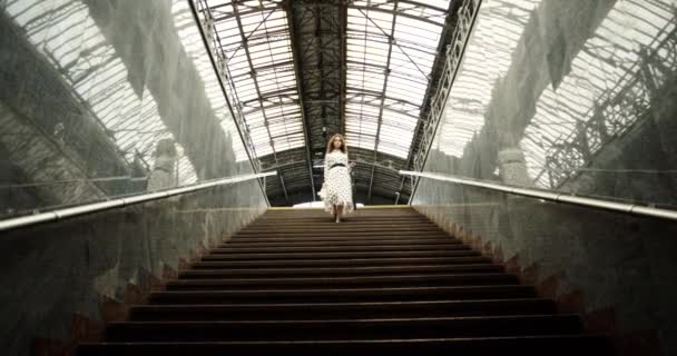 The girl in a dress descends the high stairs. bottom view. stairs at the train station. — Stock Video