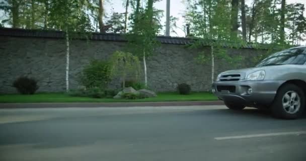 Grå bil kör på vägen. på en bakgrund av höga staket och träd. — Stockvideo