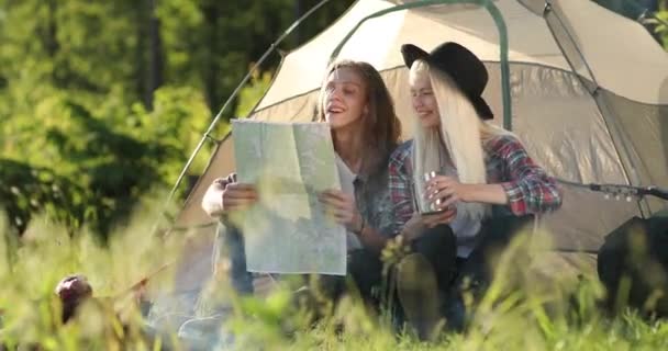 Felice giovane coppia seduta sulla natura vicino tenda e falò, guardano sulla mappa. Campeggio nella foresta. Filmati 4K. Volti sorridenti . — Video Stock