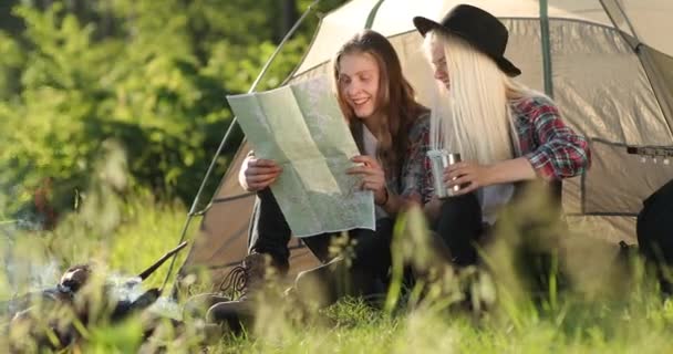 Joyeux jeune couple assis sur la nature près de la tente et du feu de camp, ils regardent sur la carte. Camping forestier. Vidéo 4K. Visages souriants . — Video