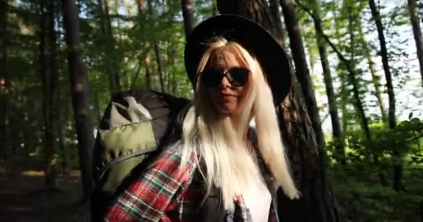 Γοητευτική νεαρή γυναίκα με υπέροχα χρυσά μαλλιά, μαύρα γυαλιά ηλίου, ελκυστική νεαρή κοπέλα είναι ψύξη για τη φύση, περπατά μέσα από δάσος με camping σακίδιο. Κάμπινγκ, Ταξίδια, Φύση, Δάσος — Αρχείο Βίντεο