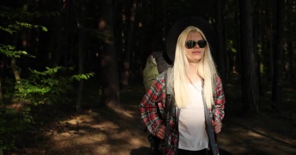 Charmante jonge vrouw met een prachtig gouden haar, zwarte zonnebril, Aantrekkelijke jonge dame is chillen op de natuur, ze lopen door het bos met camping rugzak. Camping, Reizen, Natuur, Bos — Stockvideo