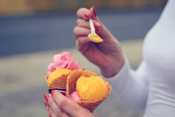 Mãos femininas segurar uma colher e sorvete colorido em cone waffle — Fotografia de Stock