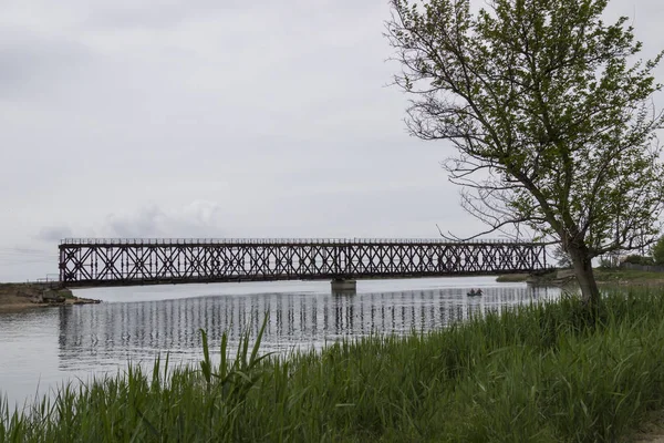 Starý železniční most přes řeku. Loď s rybáři na vodě — Stock fotografie