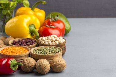 Diyet yiyecekler için bir dizi ürün. Gri arka planda, ceviz, nohut, fasulye, mercimek, sarı ve kırmızı biber, domates, avokado. Metin için bir yer var