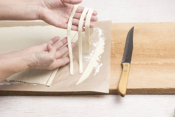 Las manos hacen pasta fresca hecha a mano. Masa laminada, cortada en tiras — Foto de Stock