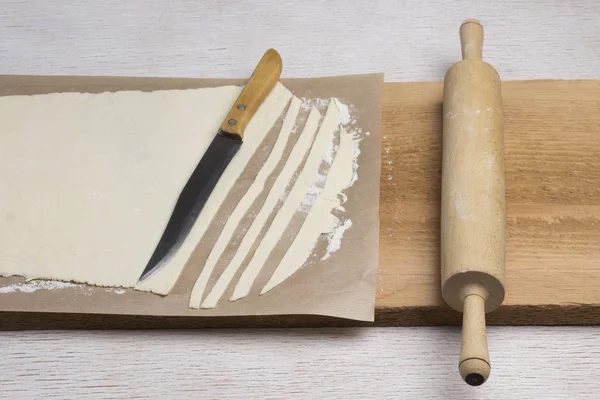 Rolled dough, sliced into strips. Rolling pin knife on cutting board — 스톡 사진
