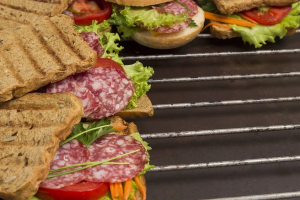 Grilled sandwich with salami, cheese tomatoes and greens on metal grill. Outdoor food concept. top view, close up